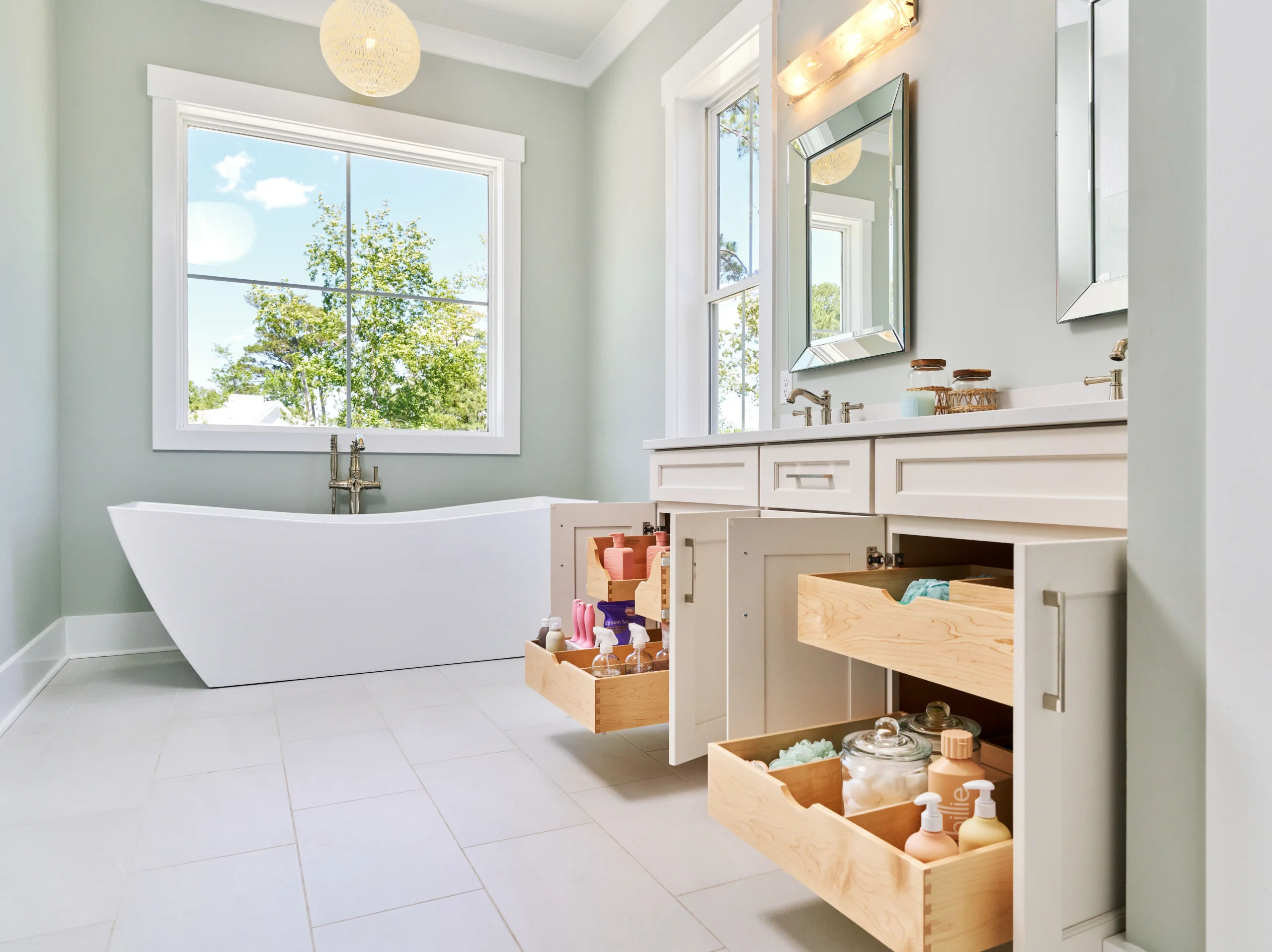 A modern bathroom with a freestanding white bathtub, a double vanity, and open cabinet drawers revealing organized toiletries