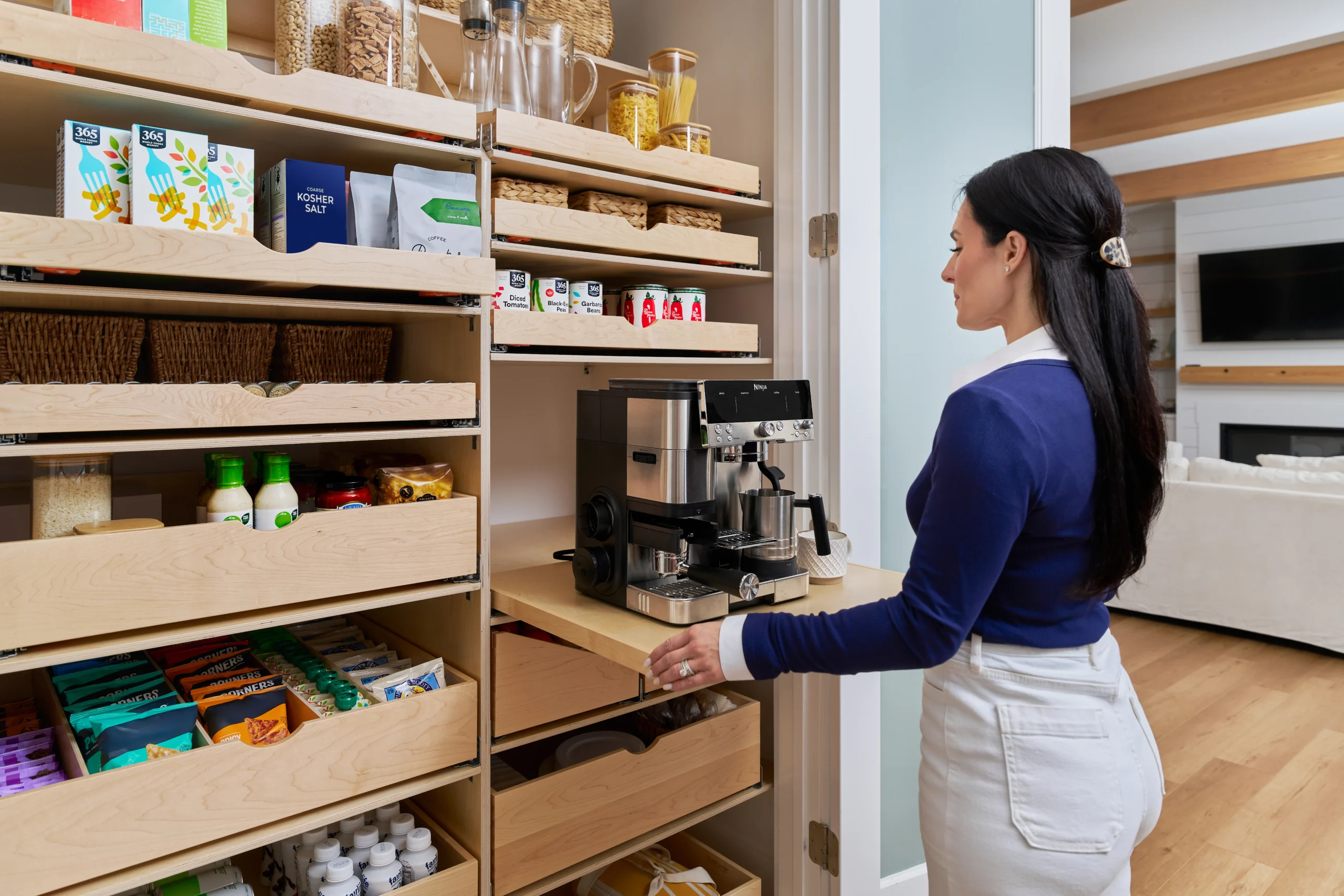 A well-organized kitchen pantry features shelves of food items, with a coffee machine prominently displayed and drawers being accessed